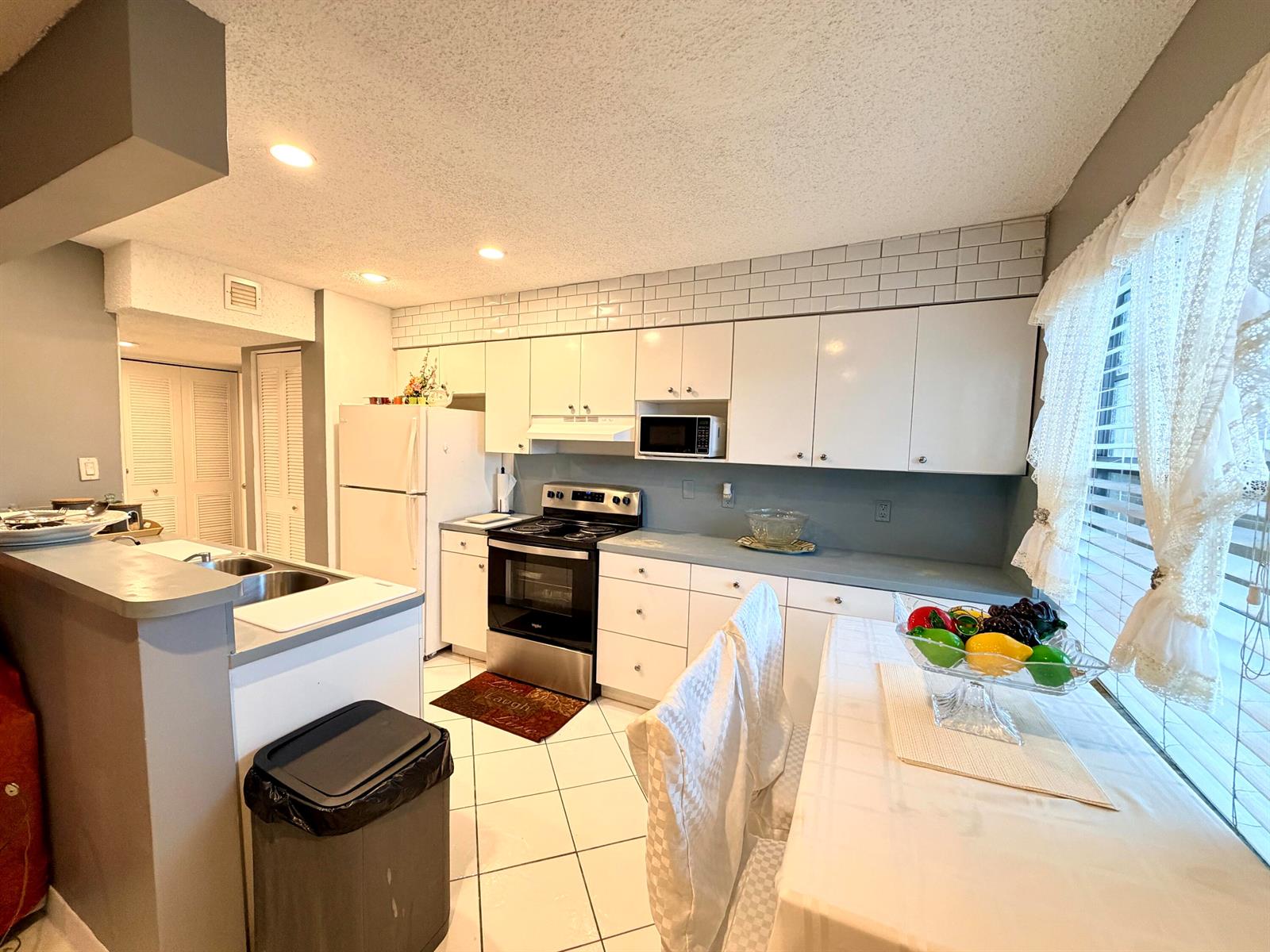 A kitchen with white cabinets, stainless steel appliances, tile flooring, and a dining area — 5180 E Sabal Palm Boulevard # 228, Tamarac FL 33319, TAMARAC, FL