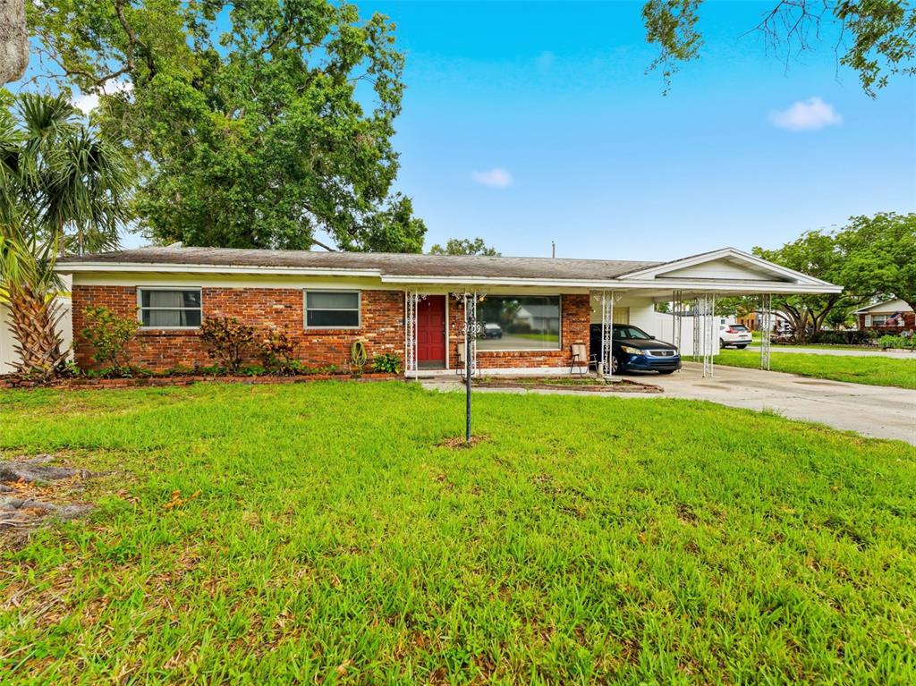 A single-story brick house with a front lawn, a red door, and an attached carport — 2109 W ERNA DRIVE, TAMPA, FL