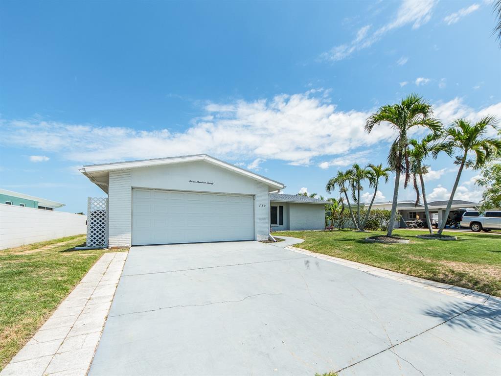 A single-story white house with a two-car garage and a paved driveway under a blue sky — 720 115TH AVENUE, TREASURE ISLAND, FL