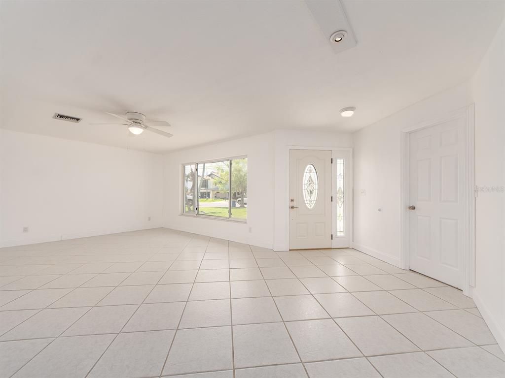 A bright, empty living room features white walls, light tile flooring, and a front door — 720 115TH AVENUE, TREASURE ISLAND, FL