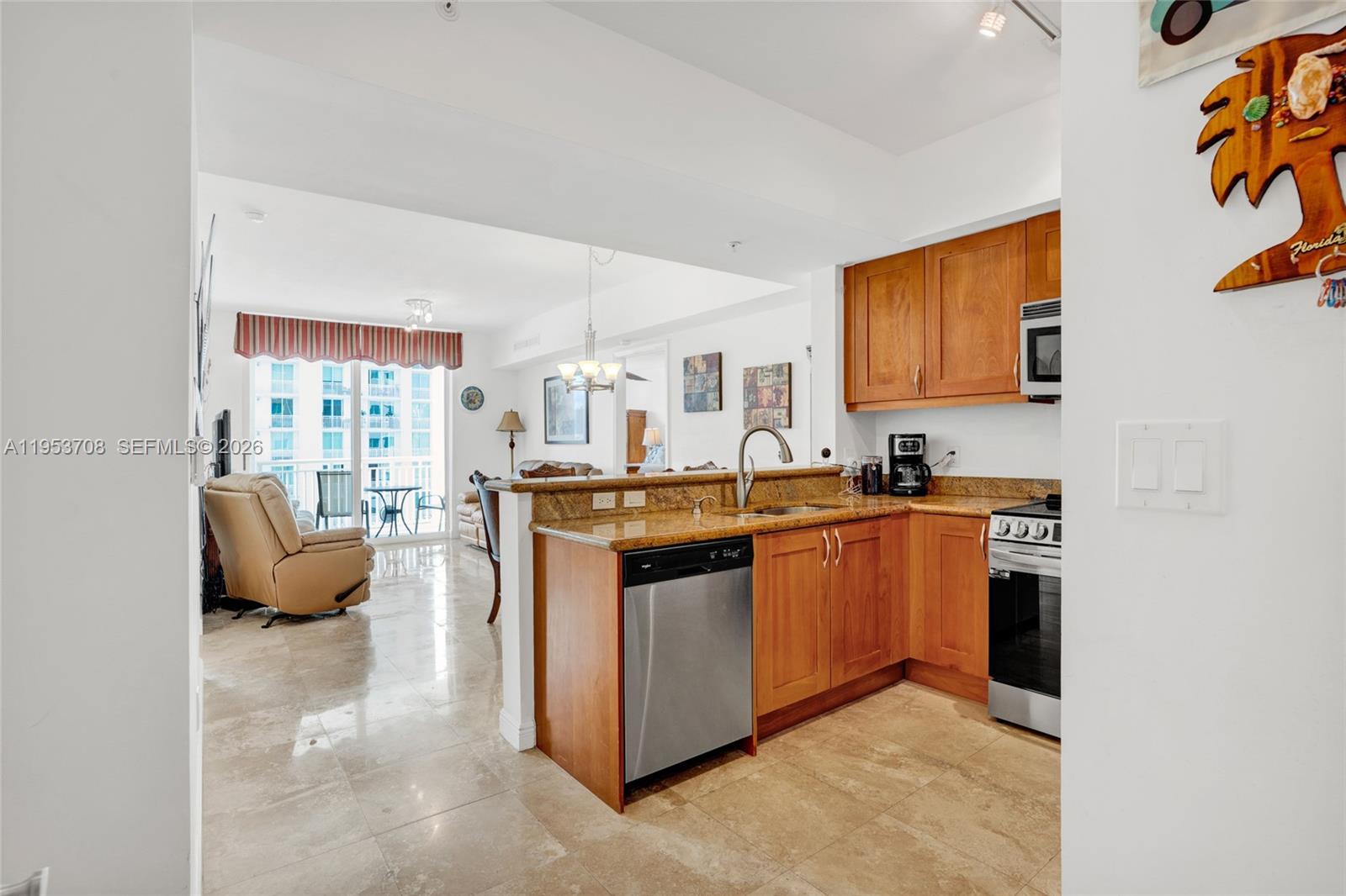 A kitchen with wood cabinets and granite countertops opens into a living area with tile floors — 1755 E Hallandale Beach Blvd # 1208E, Hallandale Beach FL 33009, HALLANDALE BEACH, FL