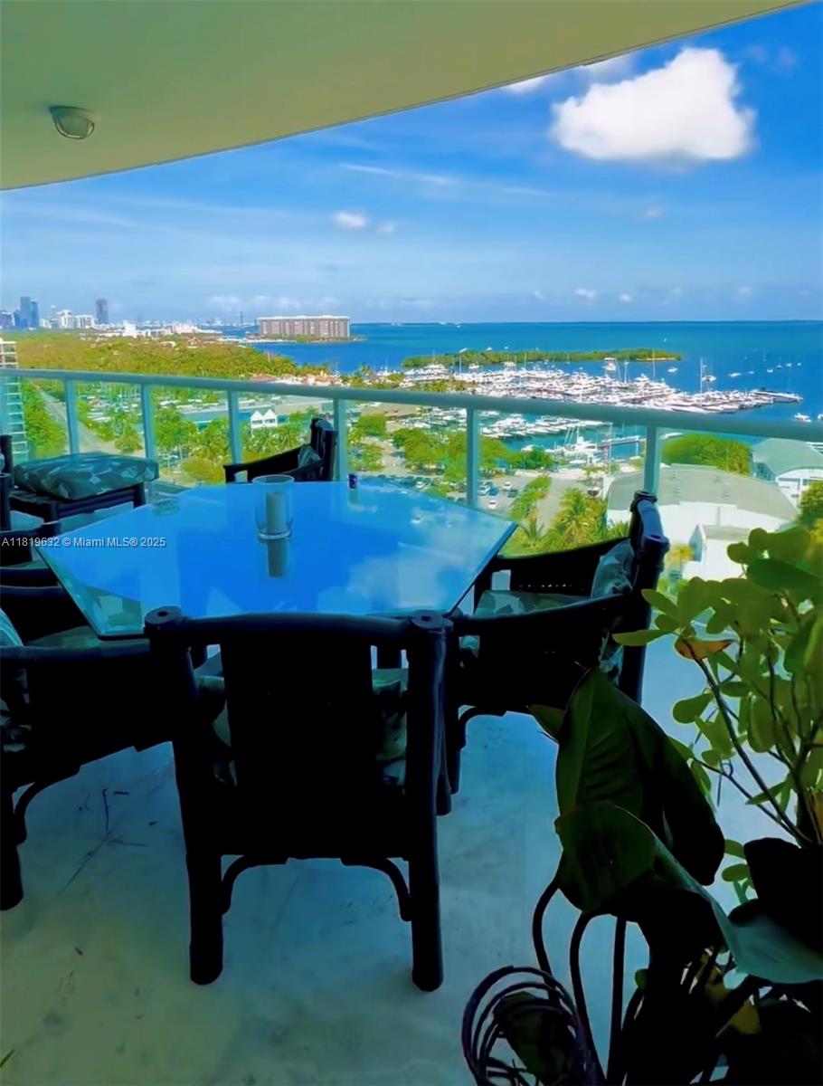 A balcony with a glass-topped table and chairs overlooks a marina and the ocean — 2645 S Bayshore Dr # 1403, Miami FL 33133, MIAMI, FL