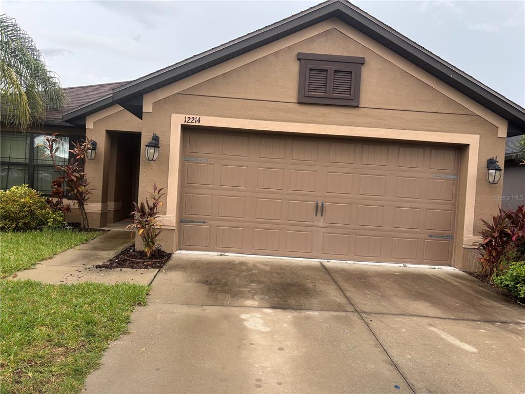 The exterior of a single-story house features a tan stucco facade and a two-car garage — 12214 LEGACY BRIGHT, RIVERVIEW, FL