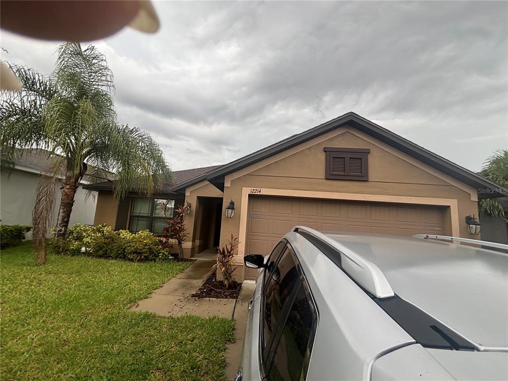 A single-story house with a tan stucco exterior, a two-car garage, and a palm tree — 12214 LEGACY BRIGHT, RIVERVIEW, FL