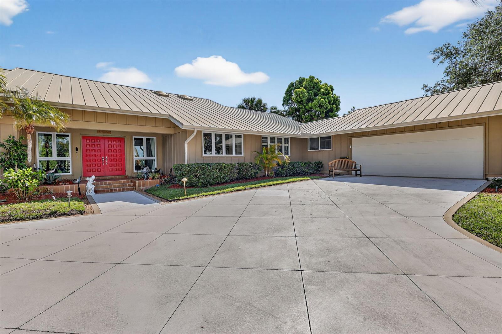 A single-story house with a metal roof, tan siding, and a red double front door — 6151 SE Winged Foot Drive, Stuart FL 34997, STUART, FL