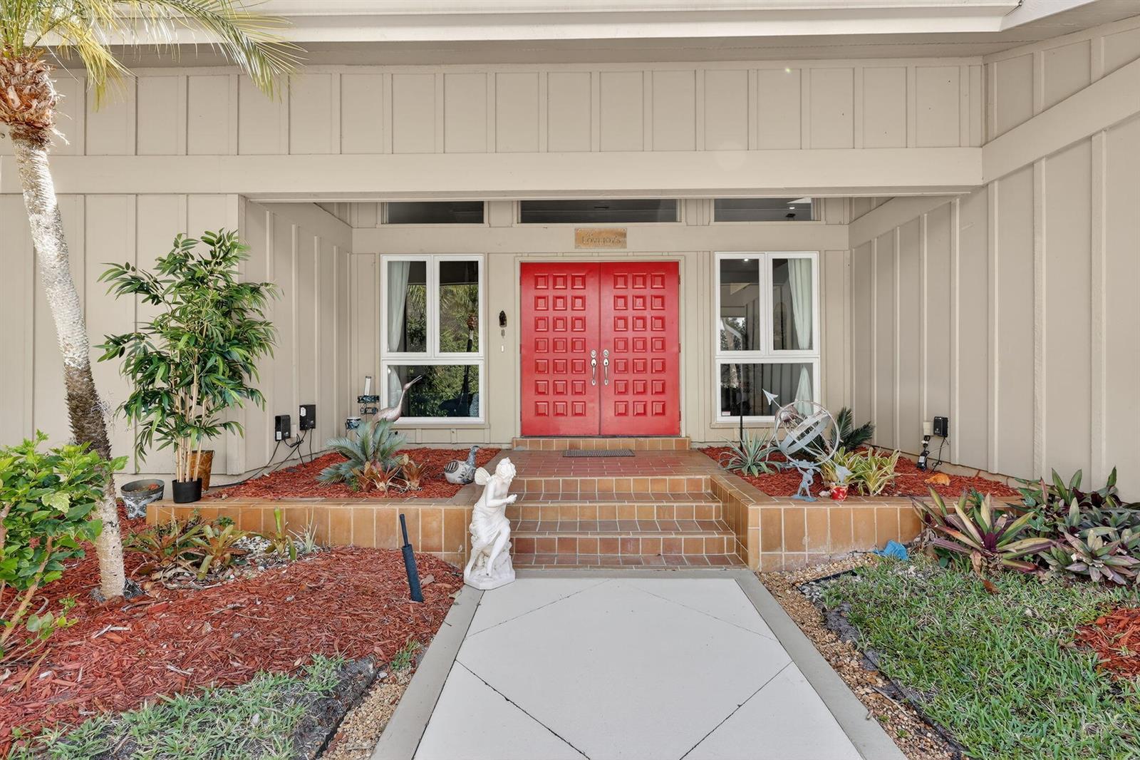 The exterior of a house features a red double door, tiled steps, and landscaping — 6151 SE Winged Foot Drive, Stuart FL 34997, STUART, FL