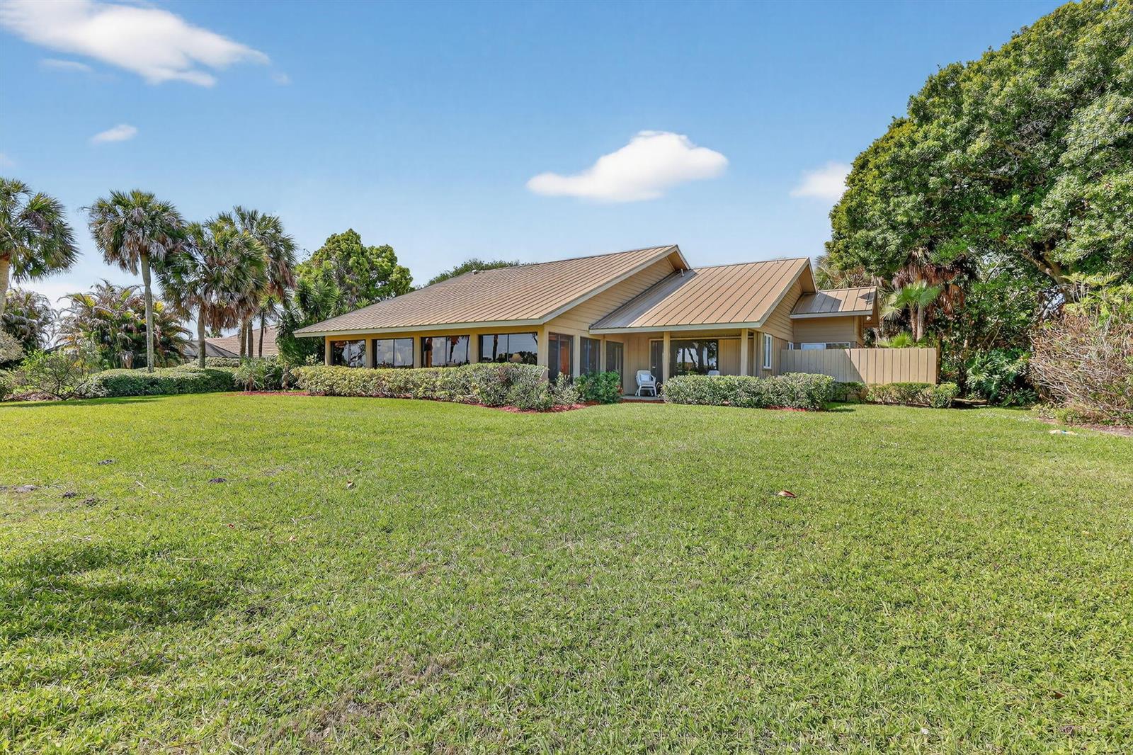 A single-story house with a metal roof sits behind a large, grassy lawn — 6151 SE Winged Foot Drive, Stuart FL 34997, STUART, FL