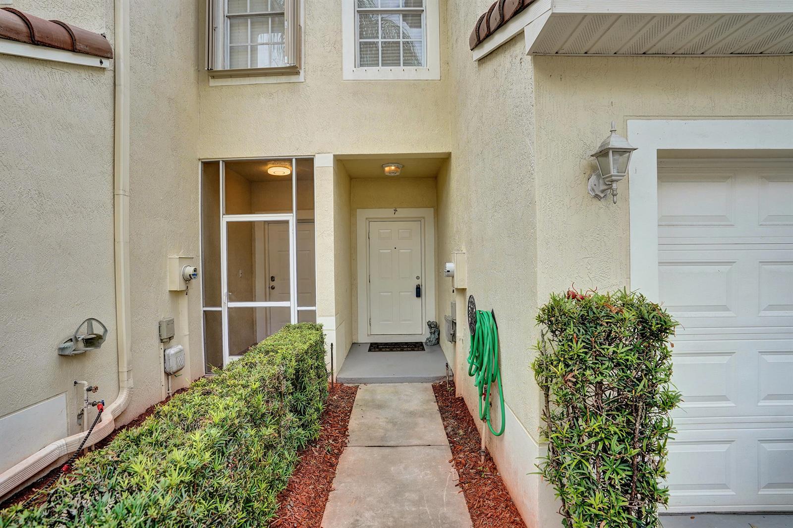 The exterior of a townhouse features a concrete walkway, a front door, and a garage — 9664 Porta Leona Lane, Boynton Beach FL 33472, BOYNTON BEACH, FL