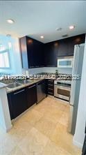 A kitchen features dark wood cabinets, stainless steel appliances, and light-colored stone tile flooring — 6515 Collins Ave # 1604, Miami Beach FL 33141, MIAMI BEACH, FL