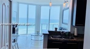 A kitchen with dark cabinets and granite countertops overlooks a living area with ocean views — 6515 Collins Ave # 1604, Miami Beach FL 33141, MIAMI BEACH, FL