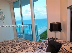 A bedroom with a patterned bedspread and a lamp overlooks the ocean from a balcony — 6515 Collins Ave # 1604, Miami Beach FL 33141, MIAMI BEACH, FL