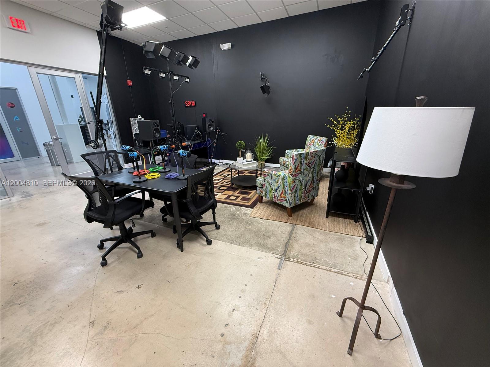 A studio room features a podcast table with microphones, patterned armchairs, and professional lighting equipment — 7445 W 4th Ave Unit 102, Hialeah FL 33014, HIALEAH, FL