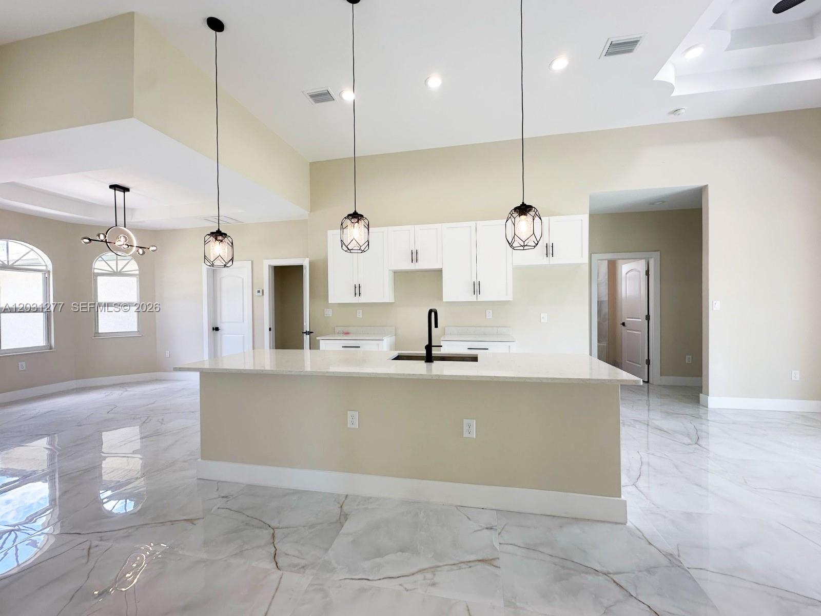A modern kitchen features white cabinets, a central island with a sink, and marble flooring — 2515 45th st W, Lehigh Acres FL 33971, LEHIGH ACRES, FL