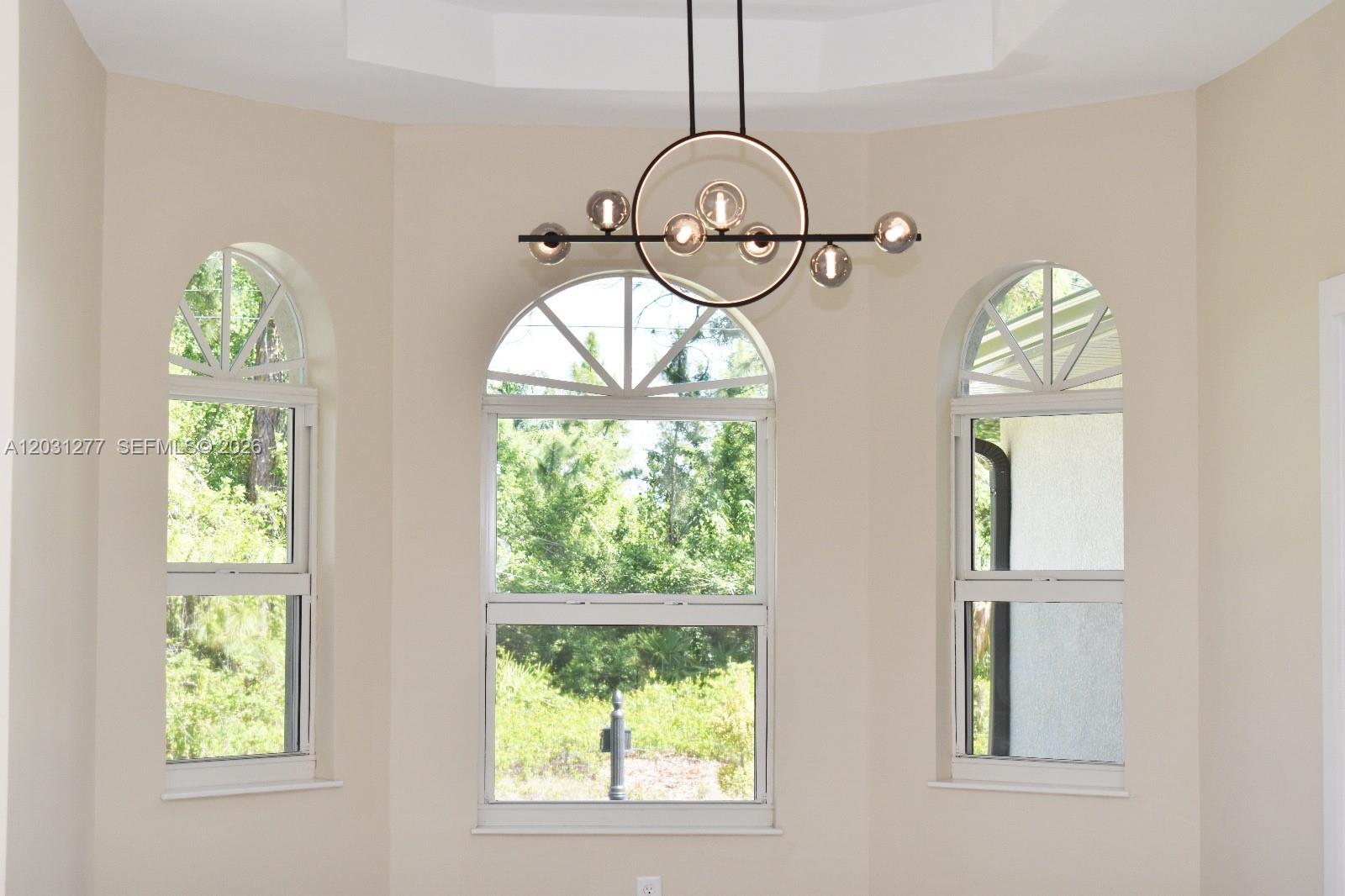 A dining nook features three arched windows, a modern circular chandelier, and beige walls — 2515 45th st W, Lehigh Acres FL 33971, LEHIGH ACRES, FL