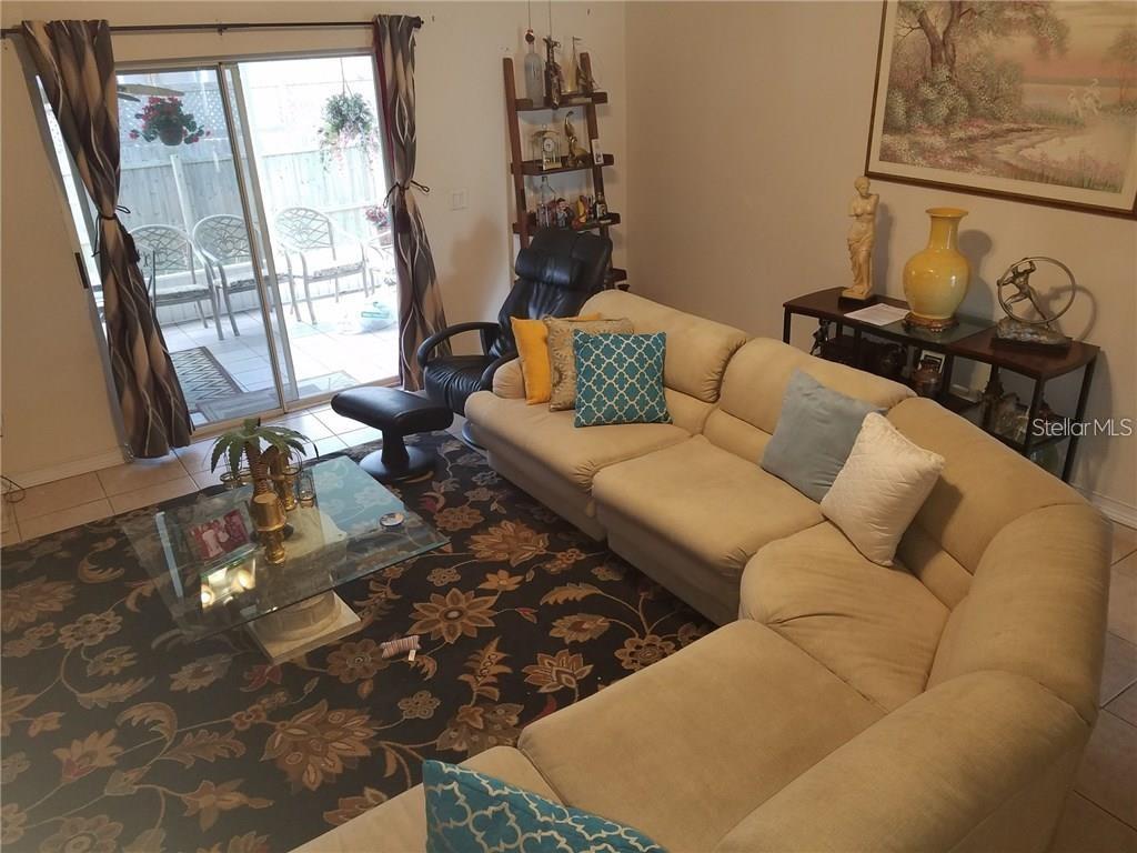 A living room features a large sectional sofa, a glass coffee table, and sliding glass doors — 3030 MUIR STREET, HOLIDAY, FL