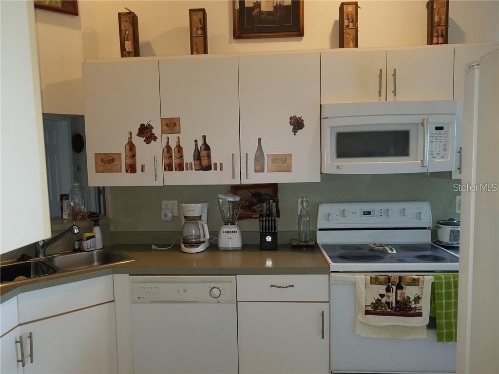 A kitchen features white cabinets, a white microwave and stove, and a stainless steel sink — 3030 MUIR STREET, HOLIDAY, FL