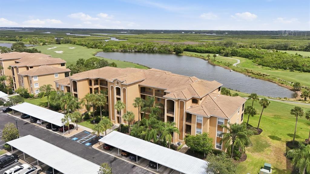 An aerial view shows a multi-story apartment building with covered parking and a nearby pond — 8309 GRAND ESTUARY TRAIL UNIT 306, BRADENTON, FL