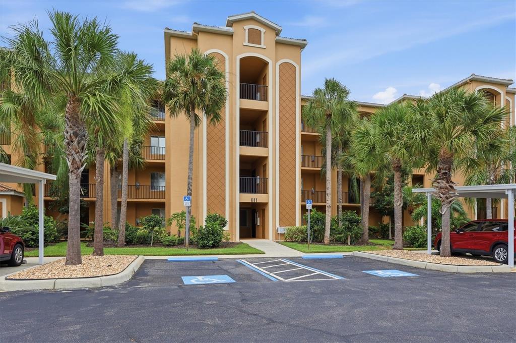 A multi-story apartment building with tan stucco walls, balconies, and accessible parking spaces in front — 8309 GRAND ESTUARY TRAIL UNIT 306, BRADENTON, FL