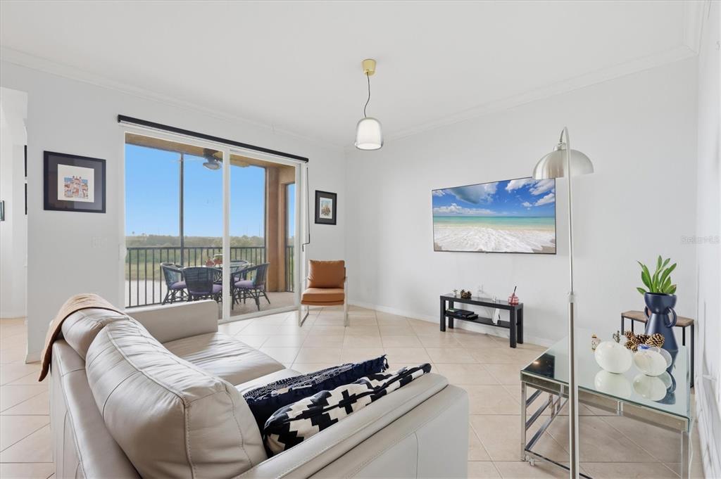 A living room with tile floors, a white sofa, a wall-mounted television, and a balcony — 8309 GRAND ESTUARY TRAIL UNIT 306, BRADENTON, FL