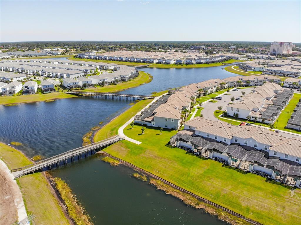 An aerial view shows a residential community with townhomes, a large lake, and pedestrian bridges — 3121 PARADOX CIRCLE UNIT 301, KISSIMMEE, FL