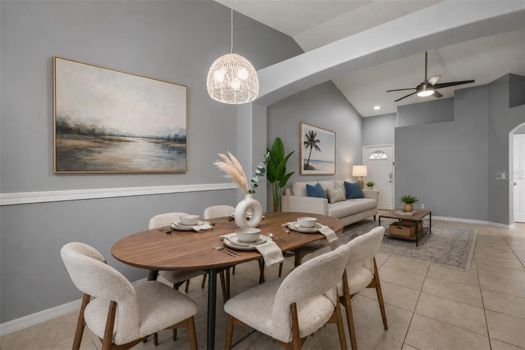 A dining area with an oval wooden table and chairs sits before a living room — 2832 OSPREY COVE PLACE UNIT 202, KISSIMMEE, FL