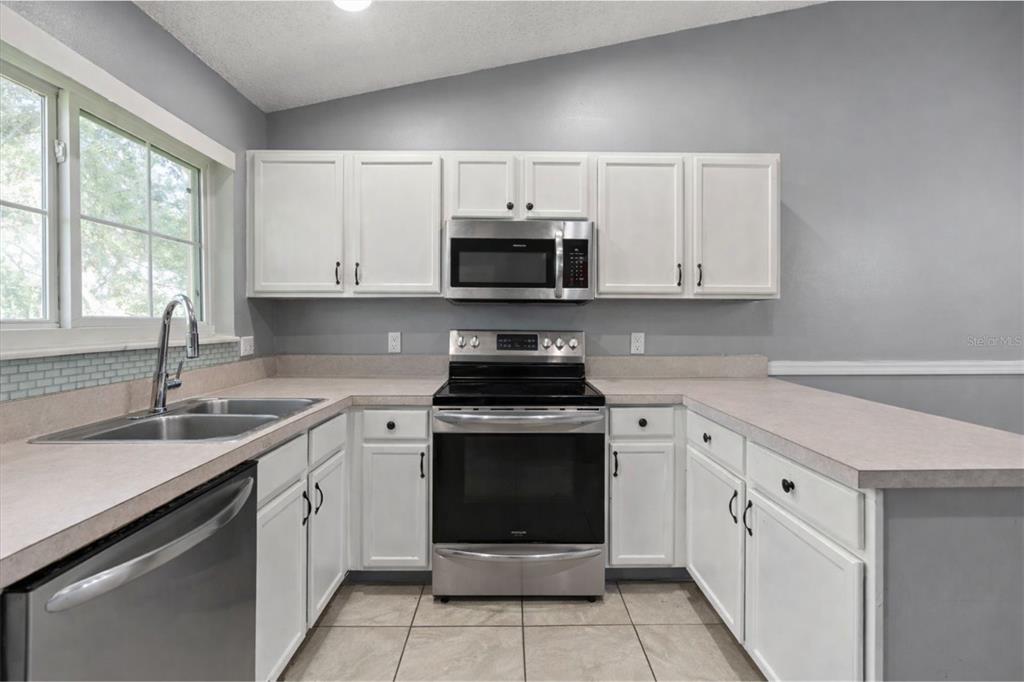 A kitchen with white cabinets, stainless steel appliances, and light-colored laminate countertops — 2832 OSPREY COVE PLACE UNIT 202, KISSIMMEE, FL
