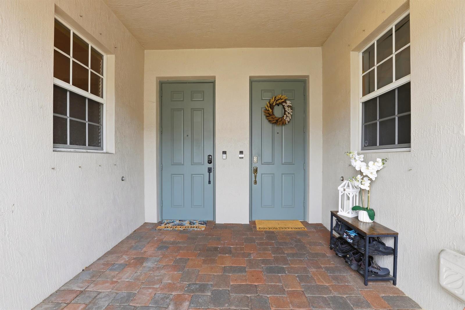 A covered entryway features two blue doors, a brick patio, and a shoe rack — 80 Nottingham Place, Boynton Beach FL 33426, BOYNTON BEACH, FL