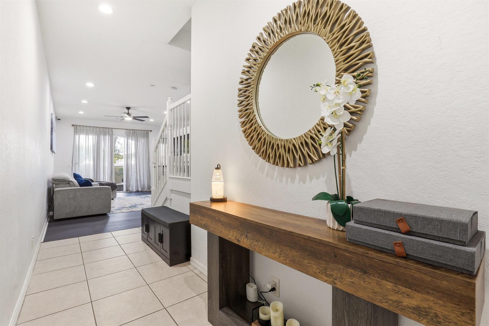 A hallway features a wooden console table, a round gold mirror, and tiled flooring — 80 Nottingham Place, Boynton Beach FL 33426, BOYNTON BEACH, FL