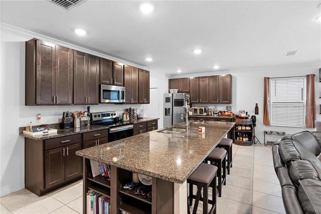 A kitchen with dark wood cabinets, granite countertops, a large island, and stainless steel appliances — 164 E FIESTA KEY LOOP, DELAND, FL