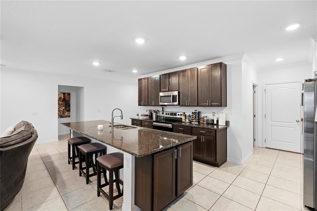A kitchen features dark wood cabinets, granite countertops, a large island, and tile flooring — 164 E FIESTA KEY LOOP, DELAND, FL