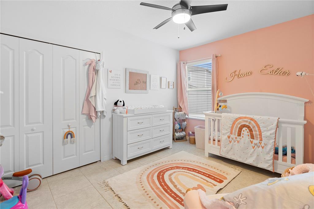 A nursery features a white crib, a matching dresser, and a rainbow rug on tile floors — 164 E FIESTA KEY LOOP, DELAND, FL
