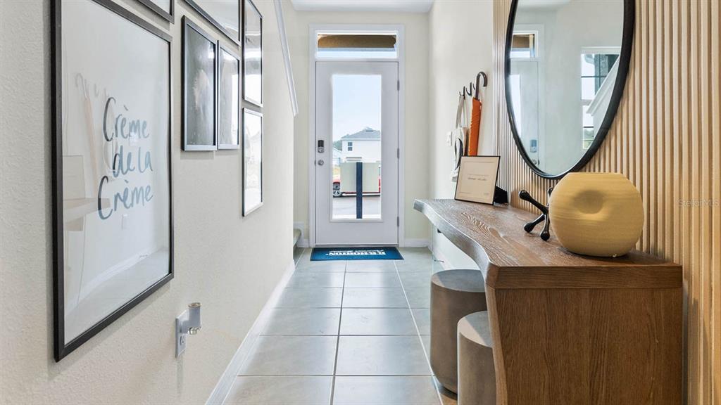 A bright entryway features tile flooring, a wooden console table, a round mirror, and wall art — 1604 SWAN SWIM DRIVE, DAVENPORT, FL