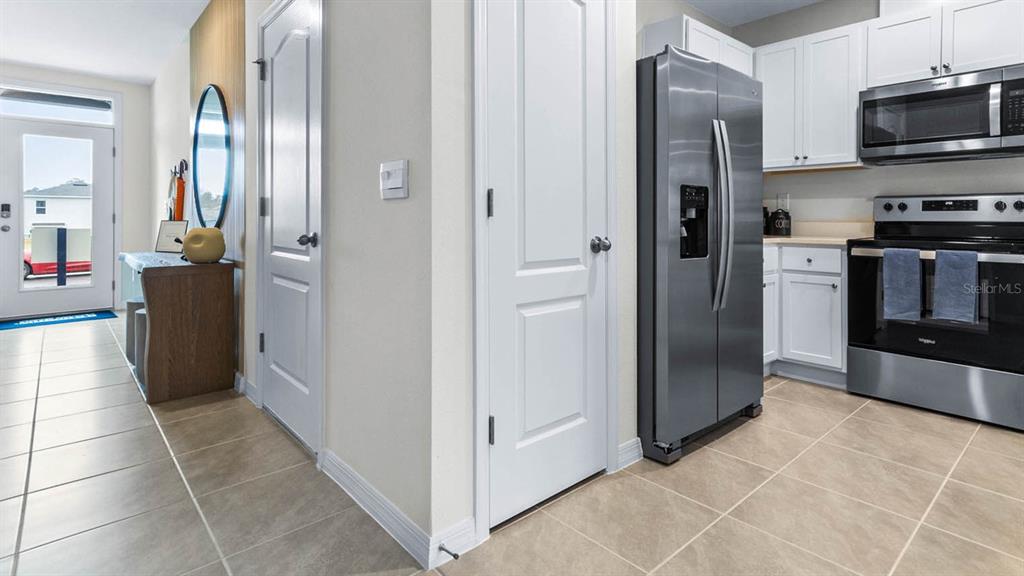 A kitchen features white cabinets, stainless steel appliances, and tile flooring near an entryway — 1604 SWAN SWIM DRIVE, DAVENPORT, FL