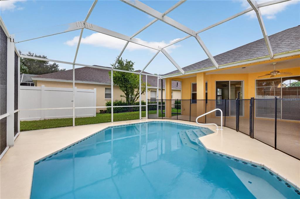 A swimming pool with a safety fence is enclosed by a screened lanai behind a house — 1549 KISH BOULEVARD, NEW PORT RICHEY, FL