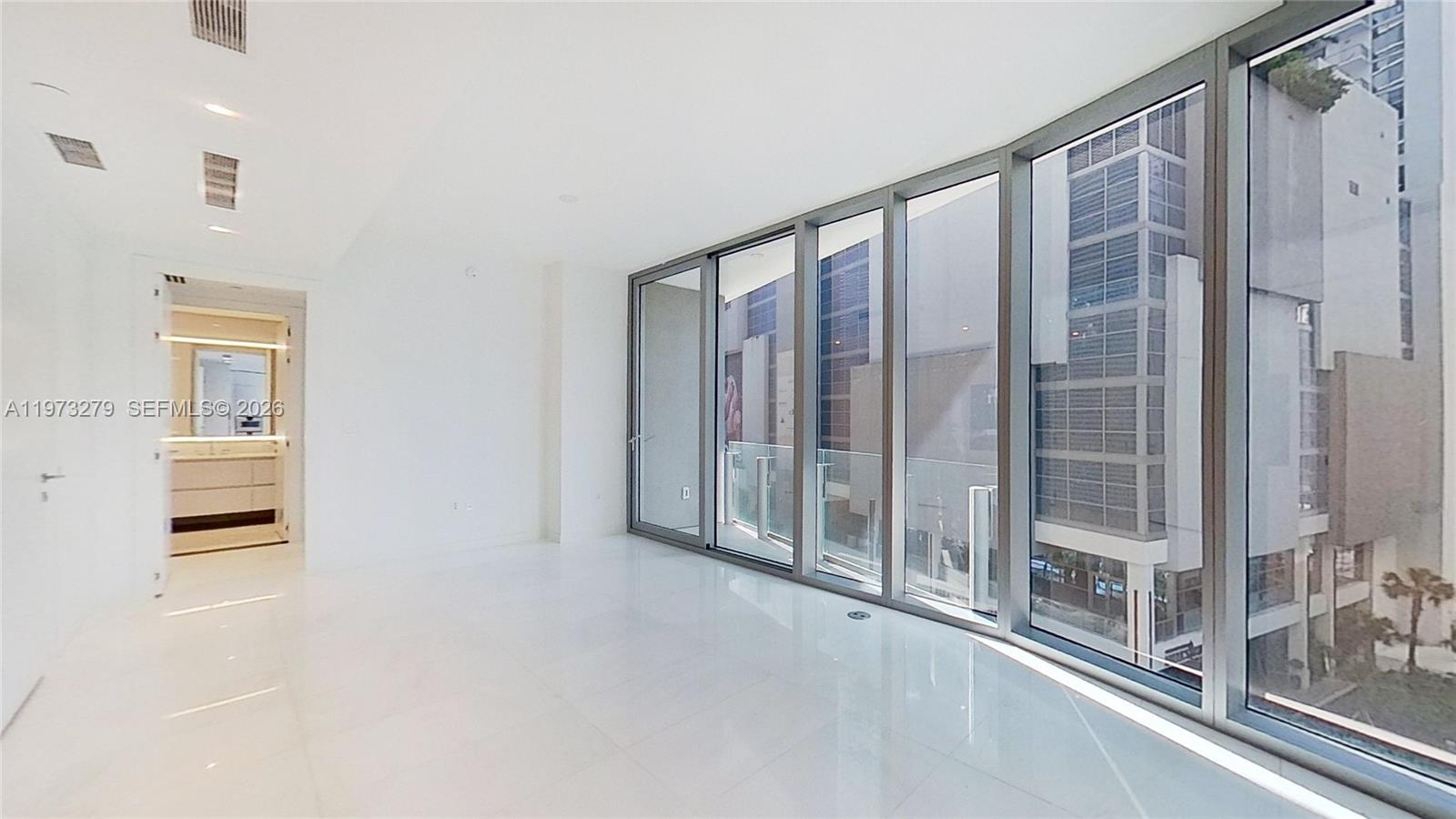 A bright, empty room features white tile floors, floor-to-ceiling windows, and an adjacent bathroom — 300 Biscayne Boulevard Way # 506E, Miami FL 33131, MIAMI, FL