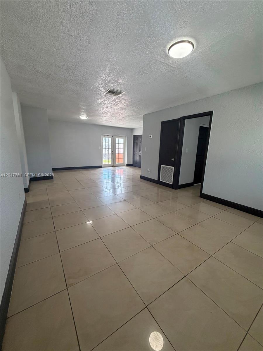 An empty room features light-colored tile flooring, gray walls, and a set of French doors — MIAMI GARDENS, FL