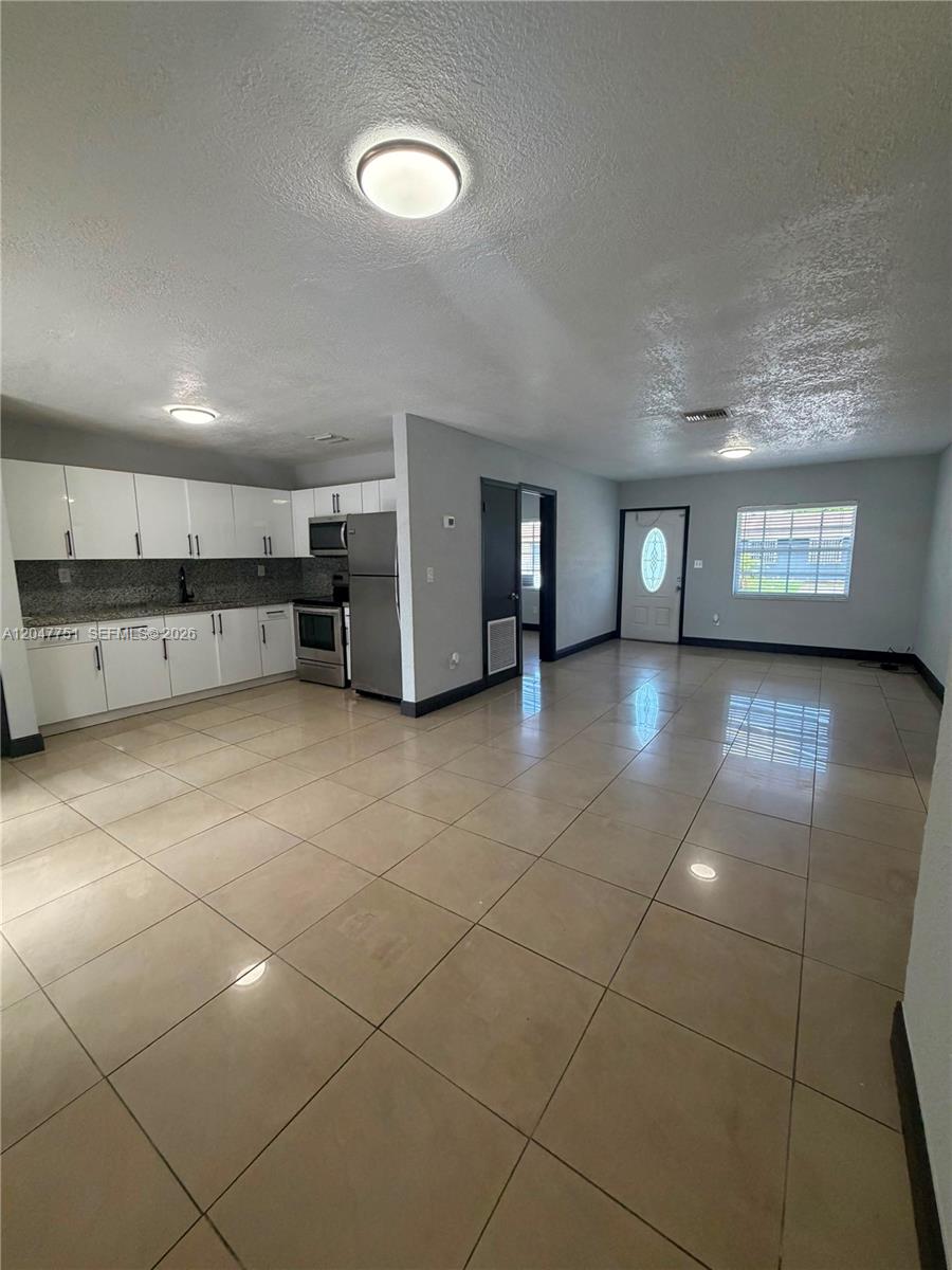 An open-concept kitchen and living area features white cabinets, stainless steel appliances, and tile flooring — MIAMI GARDENS, FL