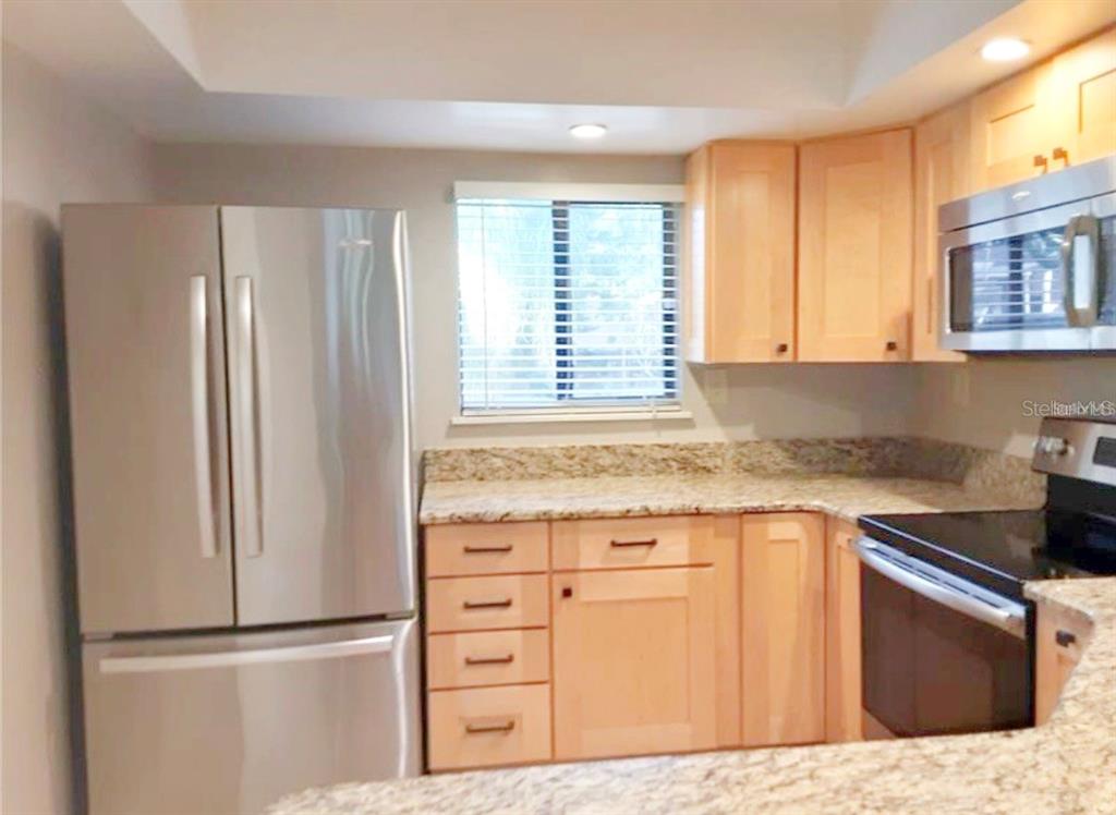 A kitchen features light wood cabinets, granite countertops, and stainless steel appliances — 1056 E MICHIGAN STREET UNIT 1056A, ORLANDO, FL