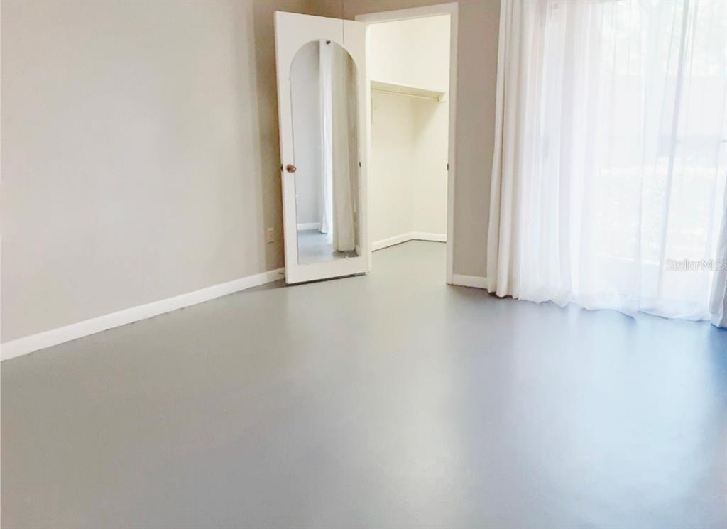 An empty room with gray flooring, a mirrored closet door, and white curtains — 1056 E MICHIGAN STREET UNIT 1056A, ORLANDO, FL