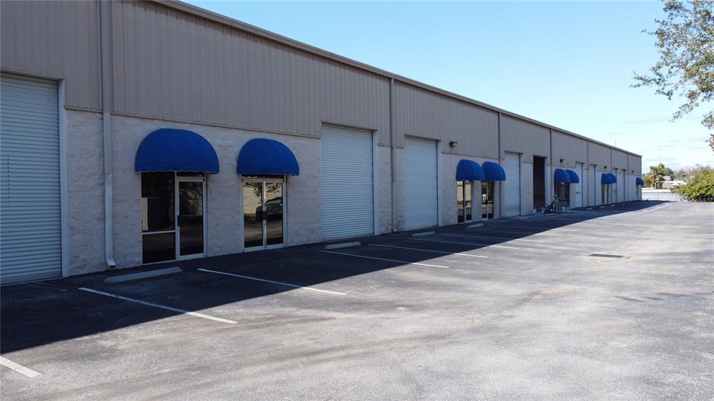 An exterior view of a long commercial warehouse building with multiple roll-up doors and awnings — 7307 SANDSCOVE COURT UNIT 5, WINTER PARK, FL