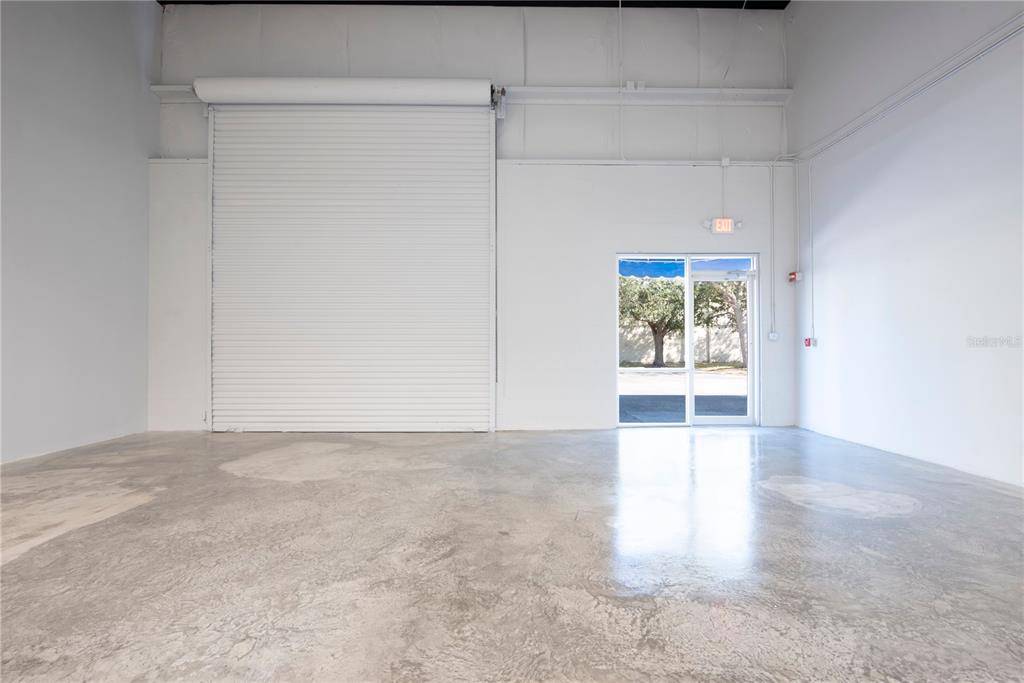 An empty warehouse space features a concrete floor, a roll-up door, and a glass door — 7307 SANDSCOVE COURT UNIT 5, WINTER PARK, FL