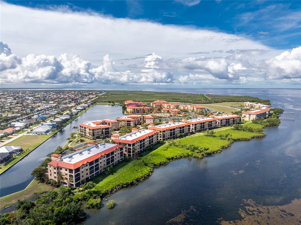 An aerial view shows a multi-story apartment complex with red roofs situated near water — 85 VIVANTE BOULEVARD UNIT 8534, PUNTA GORDA, FL
