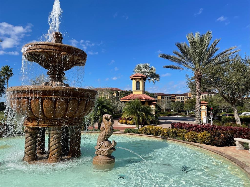 A tiered stone fountain sits in the foreground of a sunny outdoor courtyard with palm trees — 85 VIVANTE BOULEVARD UNIT 8534, PUNTA GORDA, FL