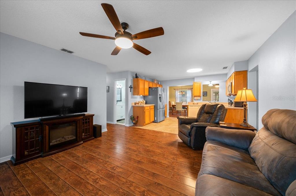 A living room with wood-look flooring, a fireplace media console, and an open kitchen beyond — 11793 SE 72ND TERRACE ROAD, BELLEVIEW, FL