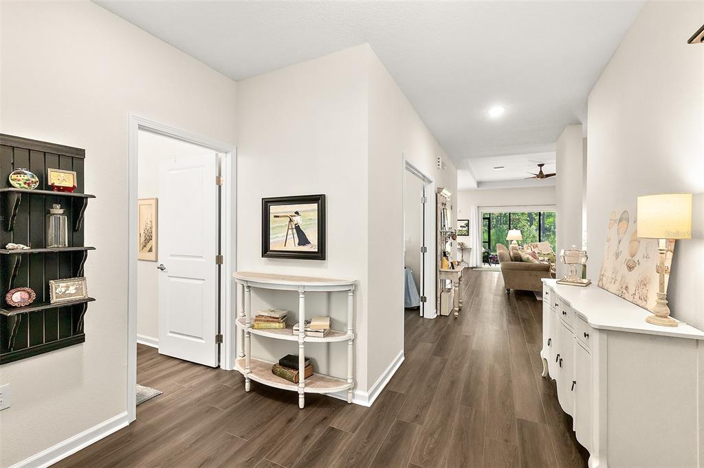 A hallway with wood-look flooring leads toward a living area with a view of trees — 8 AUCILLA PLACE, PALM COAST, FL