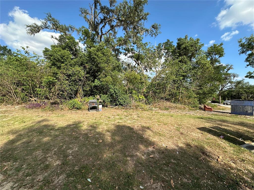 A grassy lot features a dense tree line, a small grill, and a discarded chair — 0 SHEILA LYNN COURT, DADE CITY, FL