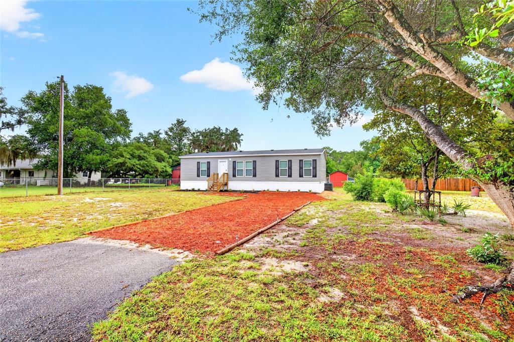 A single-story manufactured home with grey siding sits on a lot with a red-mulched driveway — 1540 SE 187TH AVENUE, SILVER SPRINGS, FL