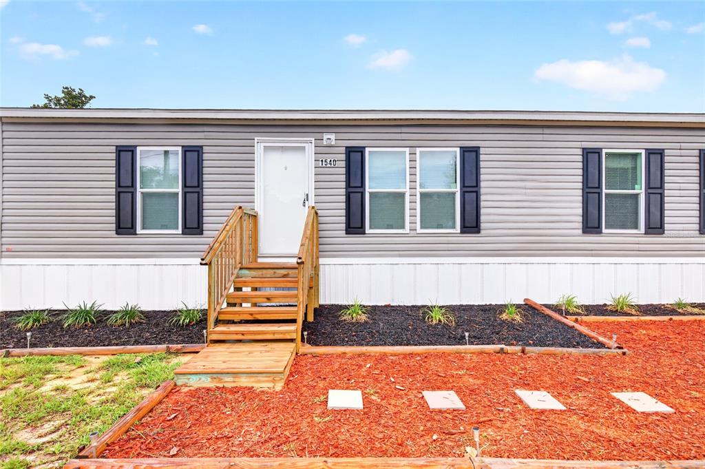 A single-story manufactured home with grey siding, black shutters, and a wooden front staircase — 1540 SE 187TH AVENUE, SILVER SPRINGS, FL