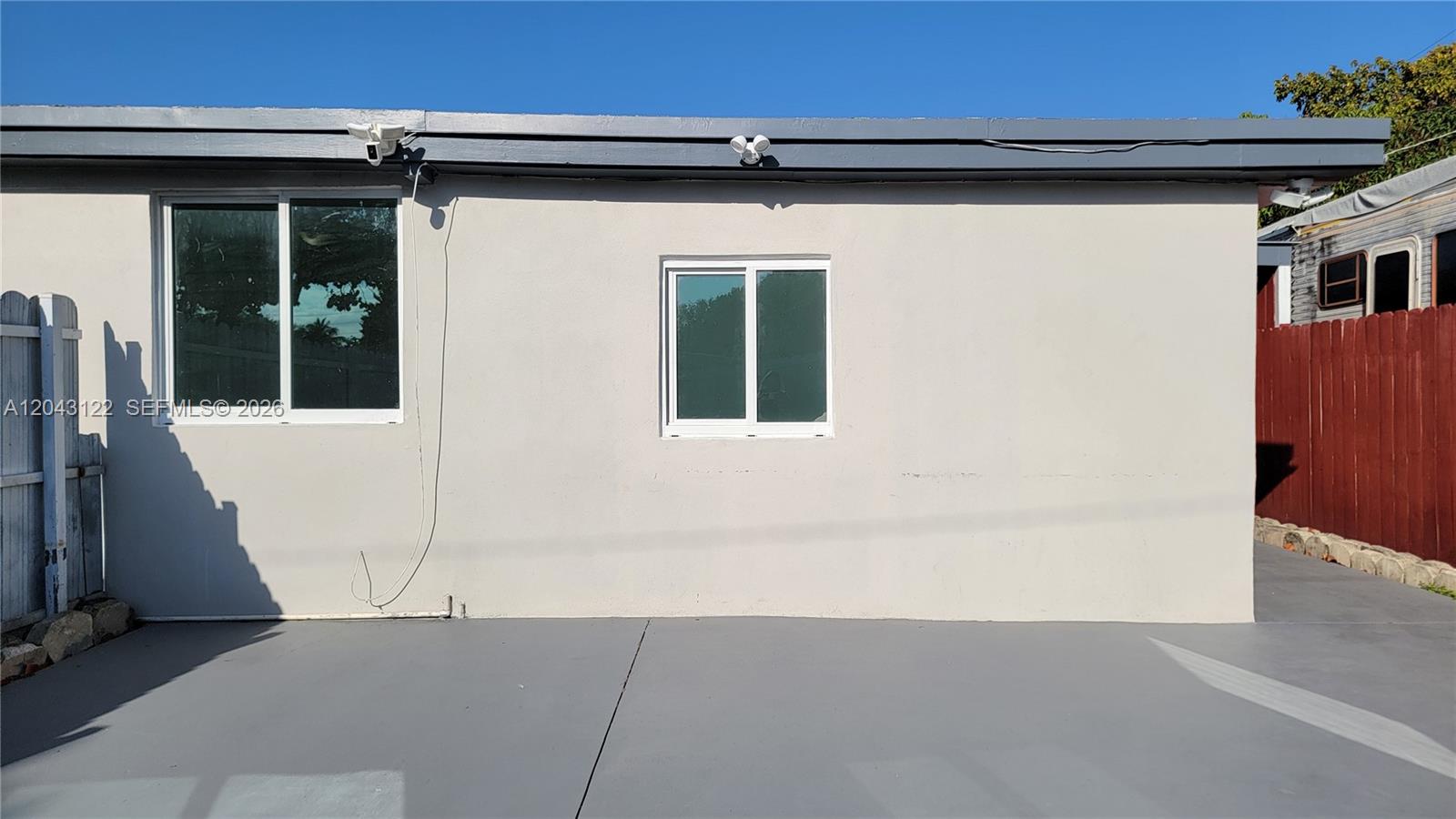 The exterior of a light-colored building features two windows, security lights, and a concrete patio — 14200 NE 15th Ave # B, North Miami FL 33161, NORTH MIAMI, FL