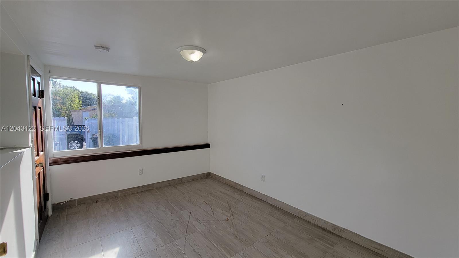 An empty room features white walls, tile flooring, a window, and a dark wood ledge — 14200 NE 15th Ave # B, North Miami FL 33161, NORTH MIAMI, FL